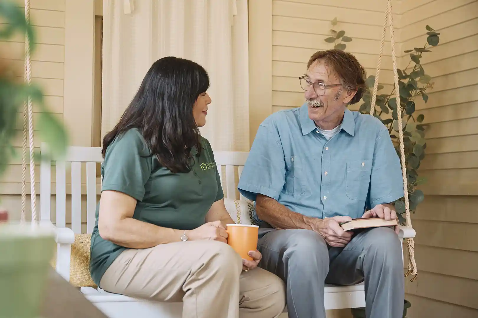 Home Instead caregiver and senior man having a warm conversation on porch swing