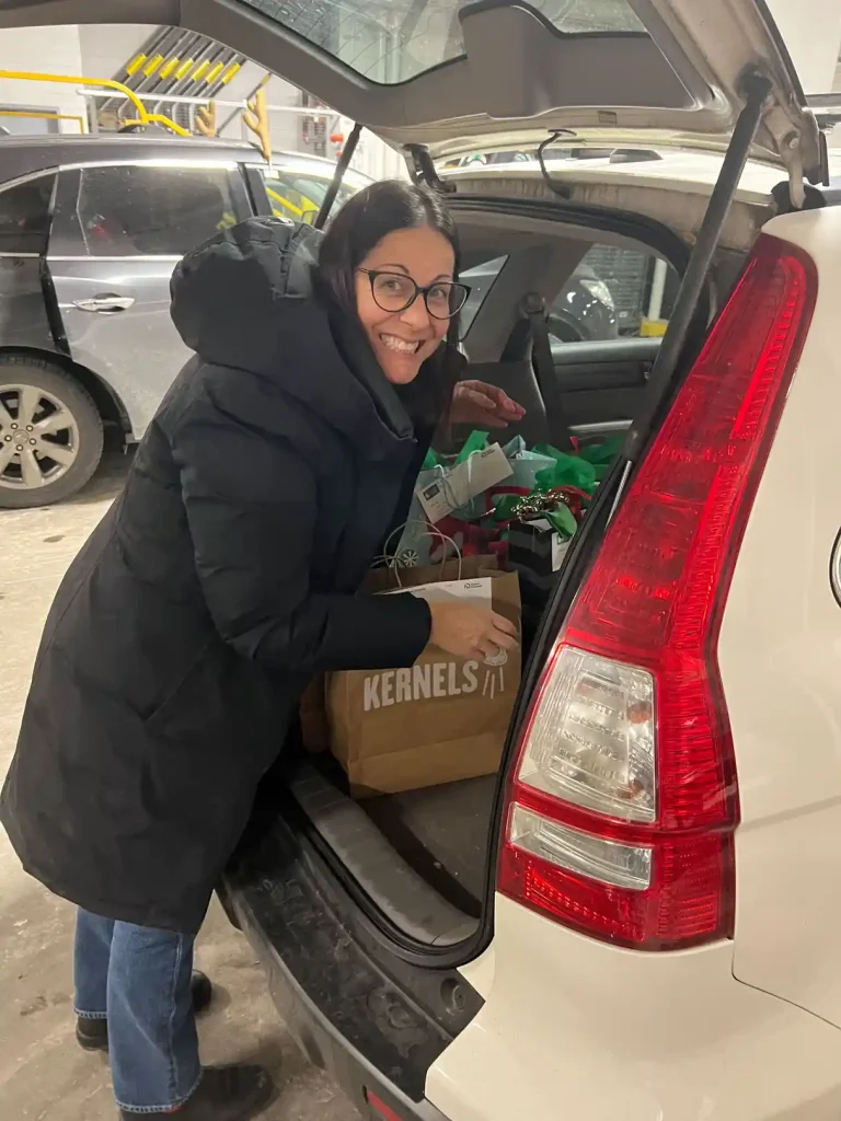 Home Instead Toronto East staff member loading holiday gift bags and boxes into vehicle trunk in underground parking garage for Be A Santa To A Senior program